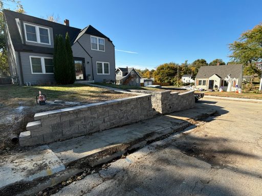 Construction scene showing a partially built stone wall beside a residential area.