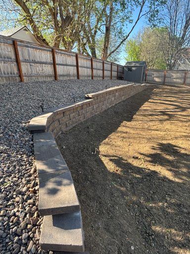 Gravel-covered backyard with a stone retaining wall and trees in the background.