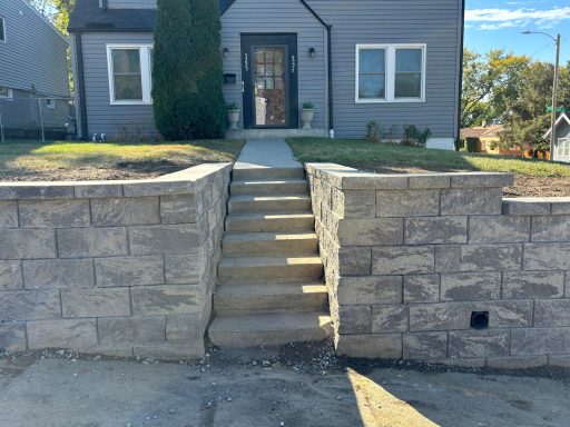 Concrete stairs leading up to a gray house with a stone wall in front.